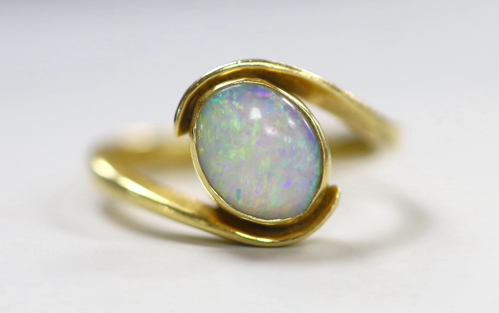 An 18ct and single stone oval white opal set ring, with crossover shoulders, size Q, gross weight 5.6 grams.